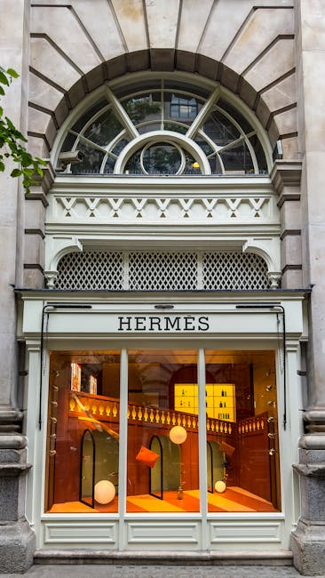 The image depicts the exterior of a building with a large, arched window set into a stone facade above a boutique storefront labeled 'HERMES.' The upper part of the window features multiple small pane
